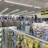 A well-lit store interior filled with fishing and outdoor equipment. The shelves are stocked with various lures, fishing lines, and other accessories. A range of colorful life vests is displayed on the back wall. A caution sign and a digital temperature display are mounted near the ceiling.